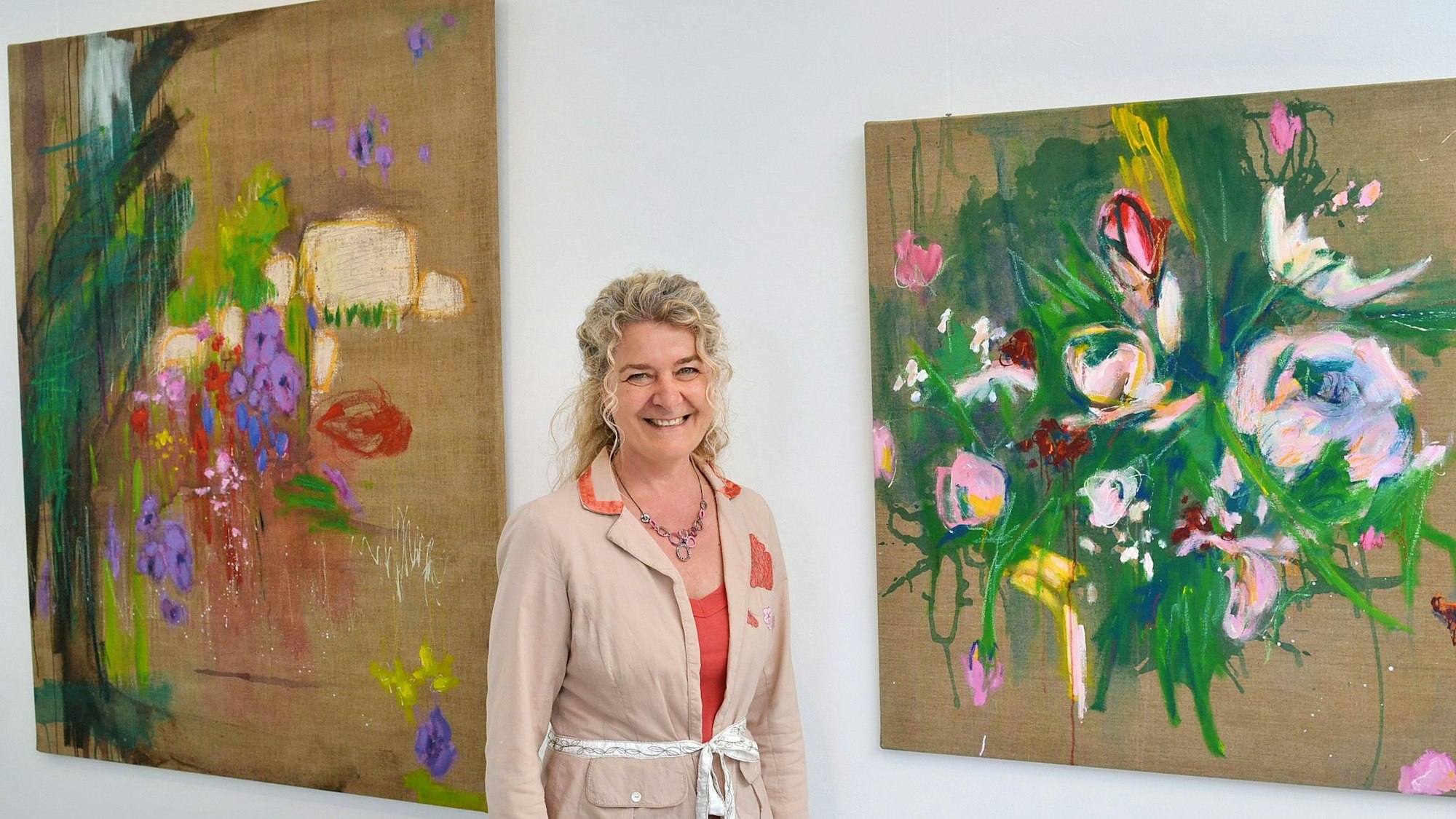Doris Maile steht vor zwei Bildern, die in intensiven Farben Pflanzen zeigen.