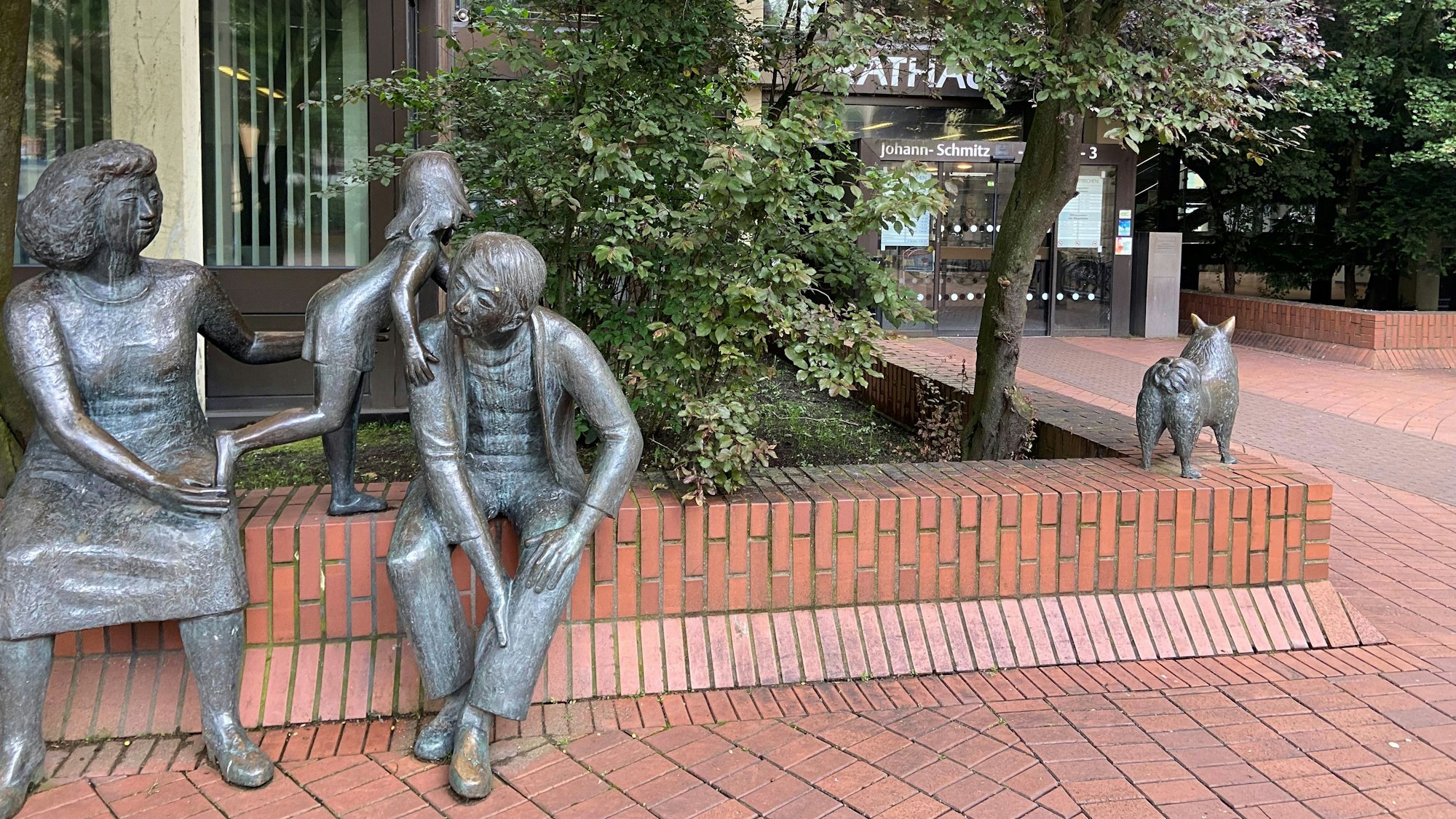 Auf dem Bild ist eine Skulpturengruppe und der Vordereingang des Rathauses zu sehen.