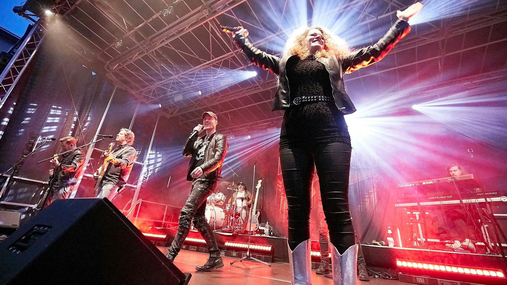 Eine Band spielt auf der Bühne, die Sängerin im Vordergrund reckt beide Arme hoch.