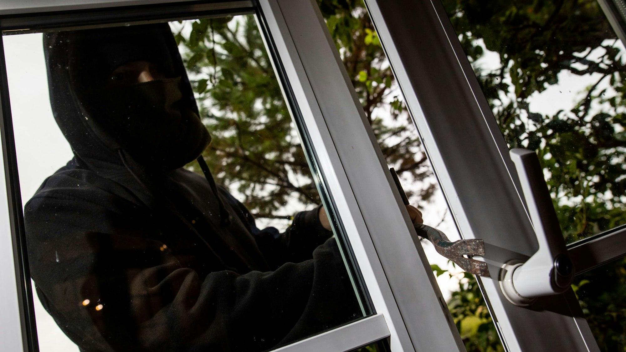 Das Bild zeigt einen maskierten Einbrecher an einer Terrassentüre.