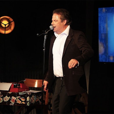 Auf einer abgedunkelten Bühne in Steinfeld steht der Sänger und Schauspieler Stephan Hippe.
