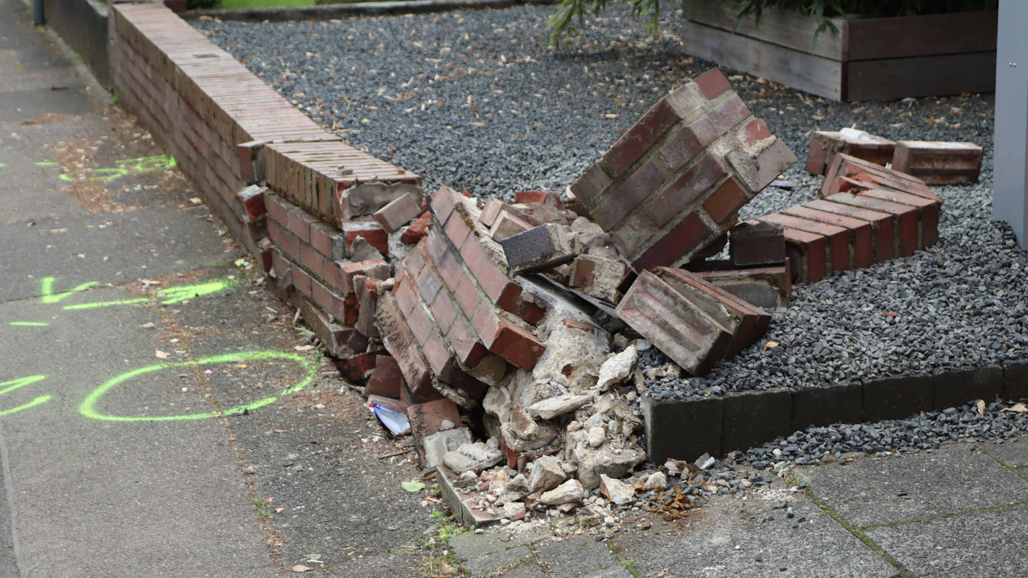 Eine Mauer aus Backstein in Trümmern. Auf dem Gehweg neongrüne Markierungen.