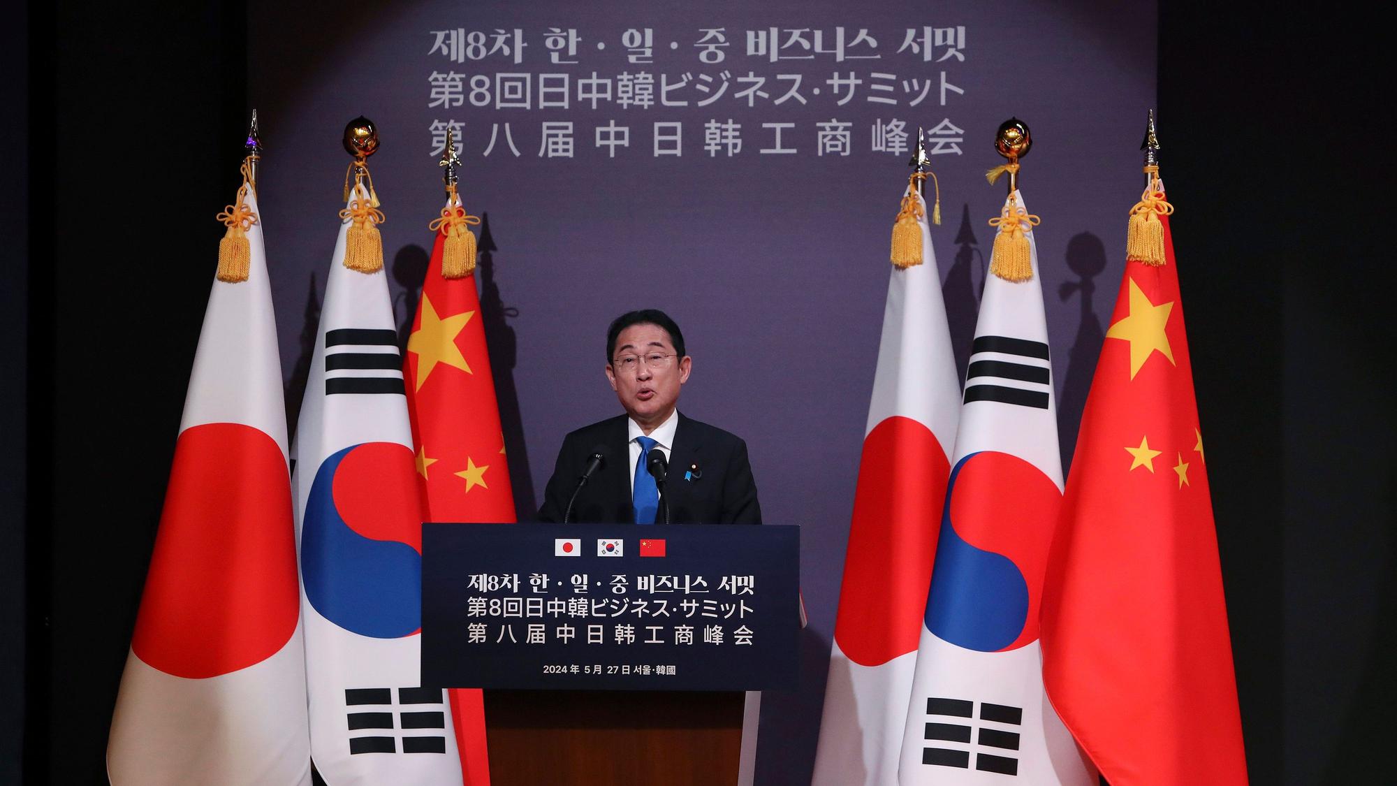 Der japanische Ministerpräsident Fumio Kishida steht an einem Rednerpult vor den Staatsflaggen von Japan, Südkorea und China.