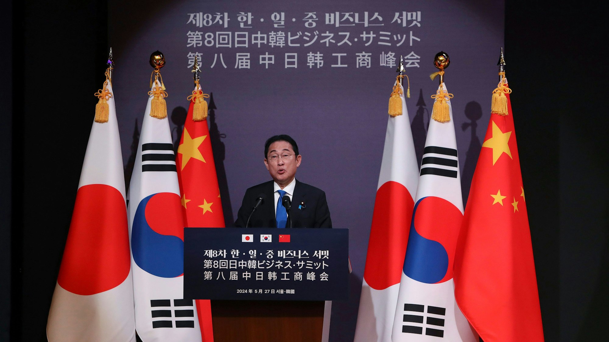 Der japanische Ministerpräsident Fumio Kishida steht an einem Rednerpult vor den Staatsflaggen von Japan, Südkorea und China.