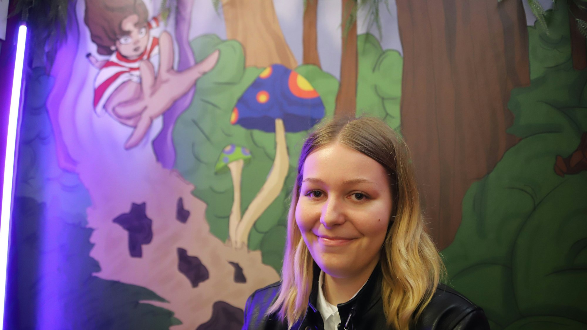 Kristina Hoffmann steht vor einer gemalten Szene aus ihrem Buch„ Amalia und die Reise durch Eldoria“.