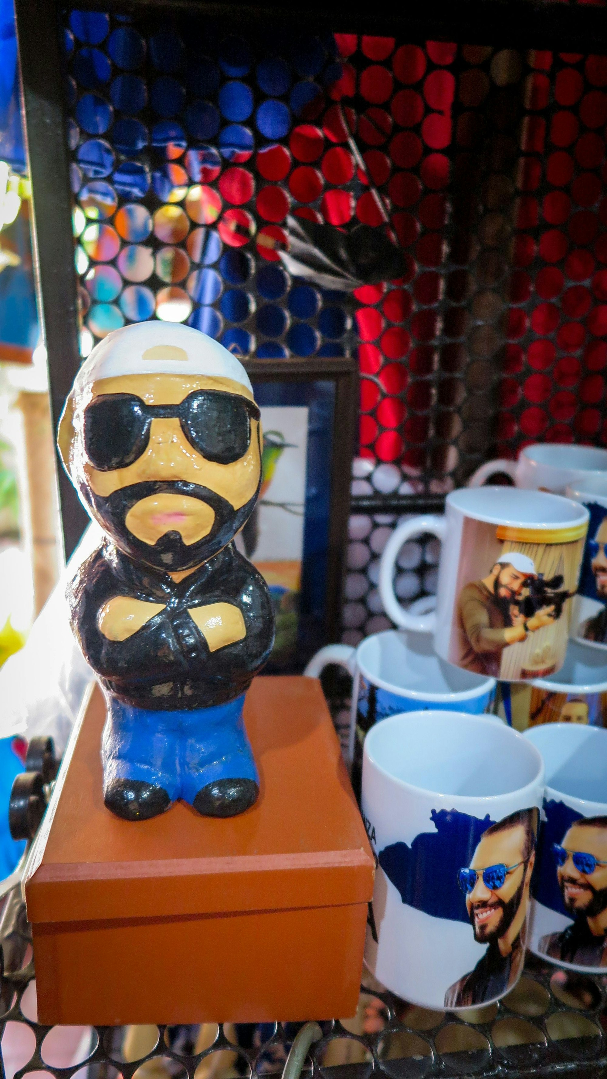 ARCHIV - 29.04.2024, El Salvador, San Salvador: Eine Sparbüchse mit der Abbildung von Präsident Bukele steht in einem Souvenirladen neben Tassen, auf denen der Staatschef mit Waffen und Sonnenbrille abgebildet ist. Für viele ist Bukele ein Volksheld. Für andere ein autoritärer Herrscher. (zu dpa: ««Coolster Diktator der Welt» tritt zweite Amtszeit in El Salvador an») Foto: Andrea Sosa Cabrios/dpa +++ dpa-Bildfunk +++