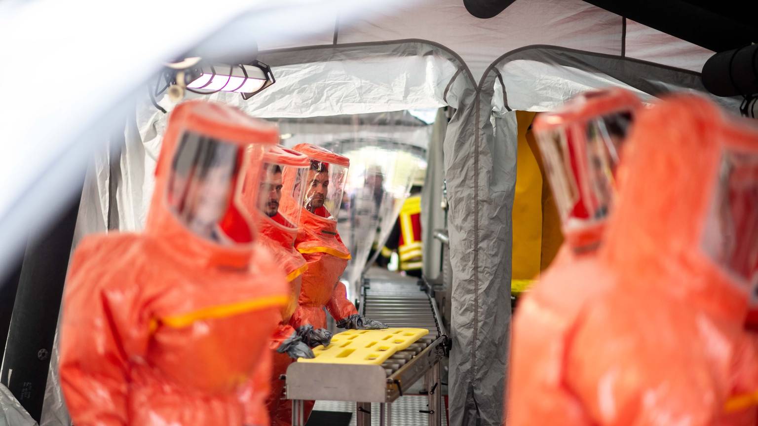 Das Bild zeigt das Zelt, in dem kontaminierte Menschen dekontaminiert werden. Zahlreiche Einsatzkräfte tragen orangefarbene Schutzanzüge.