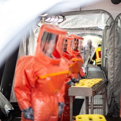 Das Bild zeigt das Zelt, in dem kontaminierte Menschen dekontaminiert werden. Zahlreiche Einsatzkräfte tragen orangefarbene Schutzanzüge.