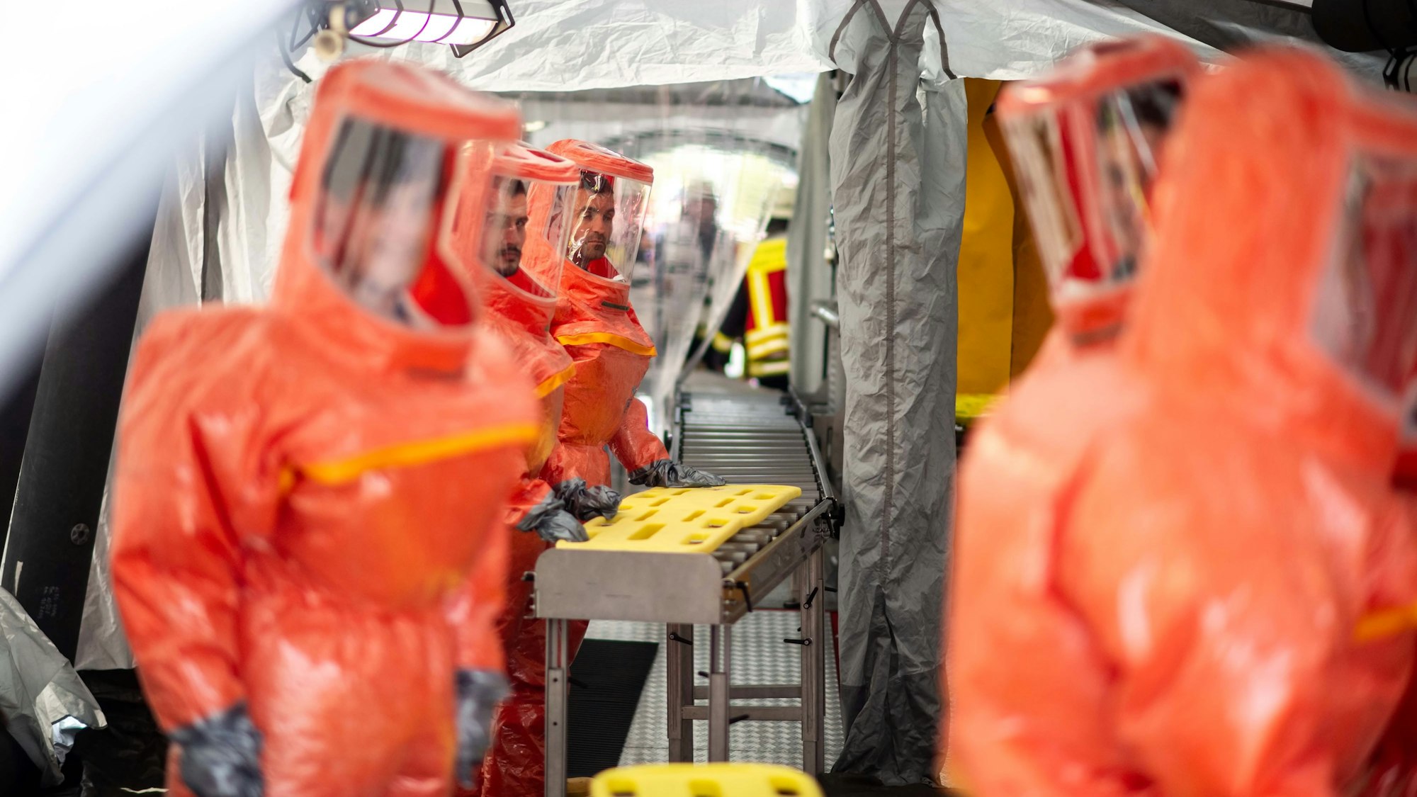 Das Bild zeigt das Zelt, in dem kontaminierte Menschen dekontaminiert werden. Zahlreiche Einsatzkräfte tragen orangefarbene Schutzanzüge.
