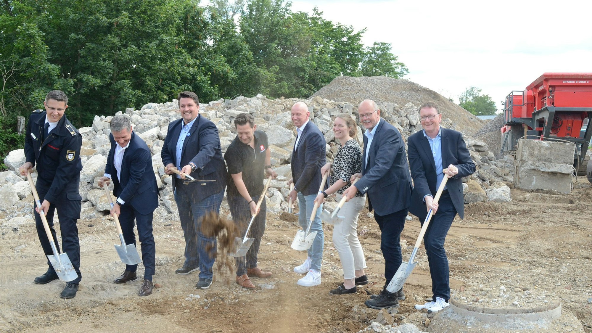 Sieben Männer und eine Frau auf einer Baustelle. Mit Spaten werfen sie Erde in die Luft.