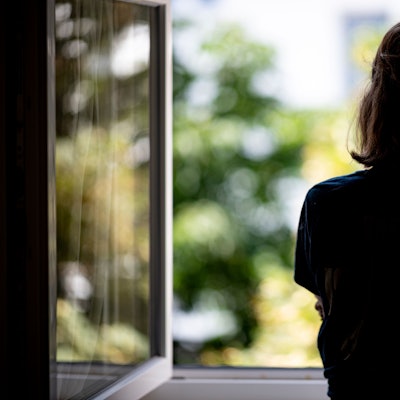 Eine Frau steht in ihrer Wohnung an einem Fenster. (Symbolbild)