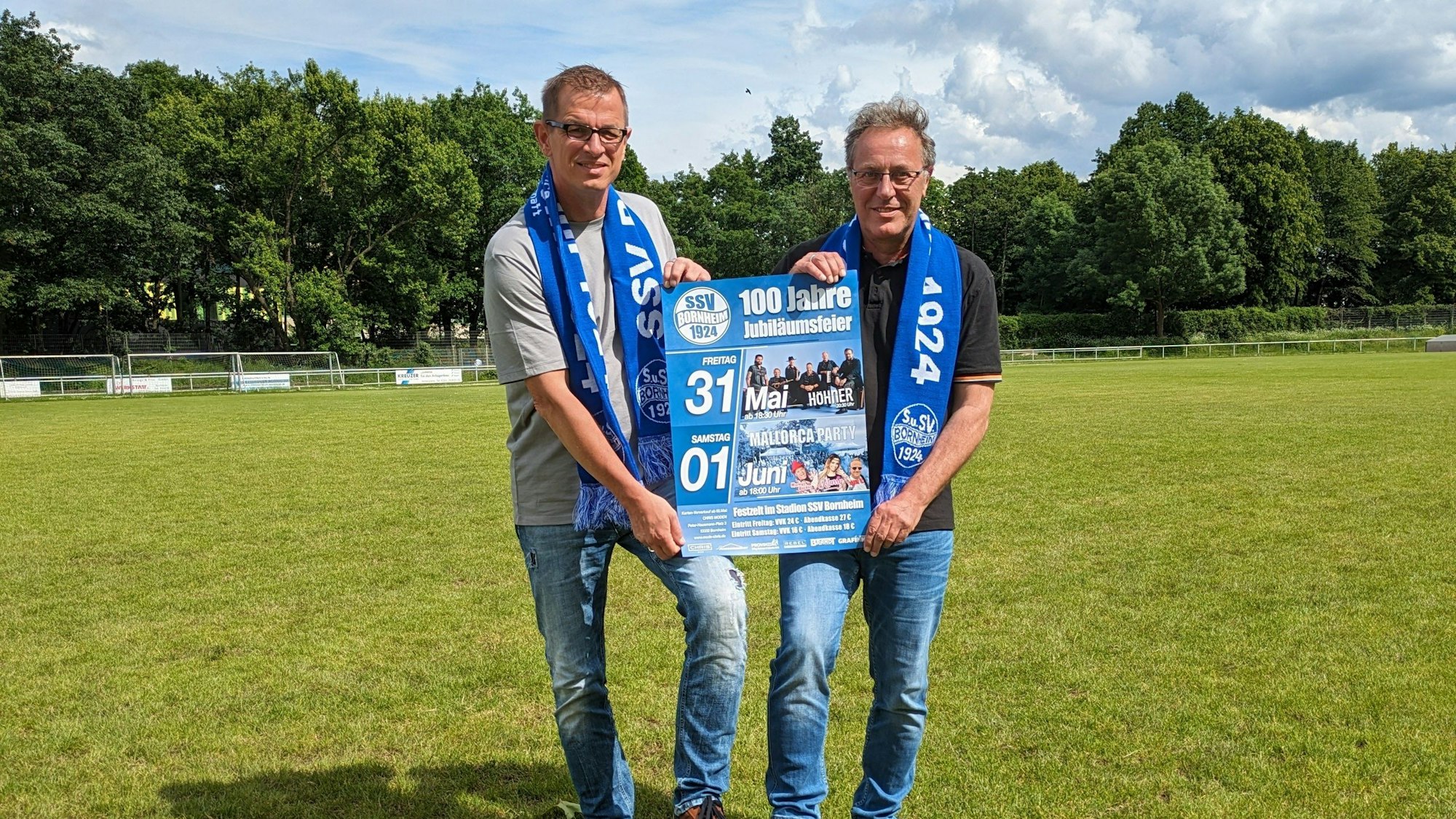 Claus Böiing (rechts) und Peter Weiler stehen mit einem Festplakat im Stadion.