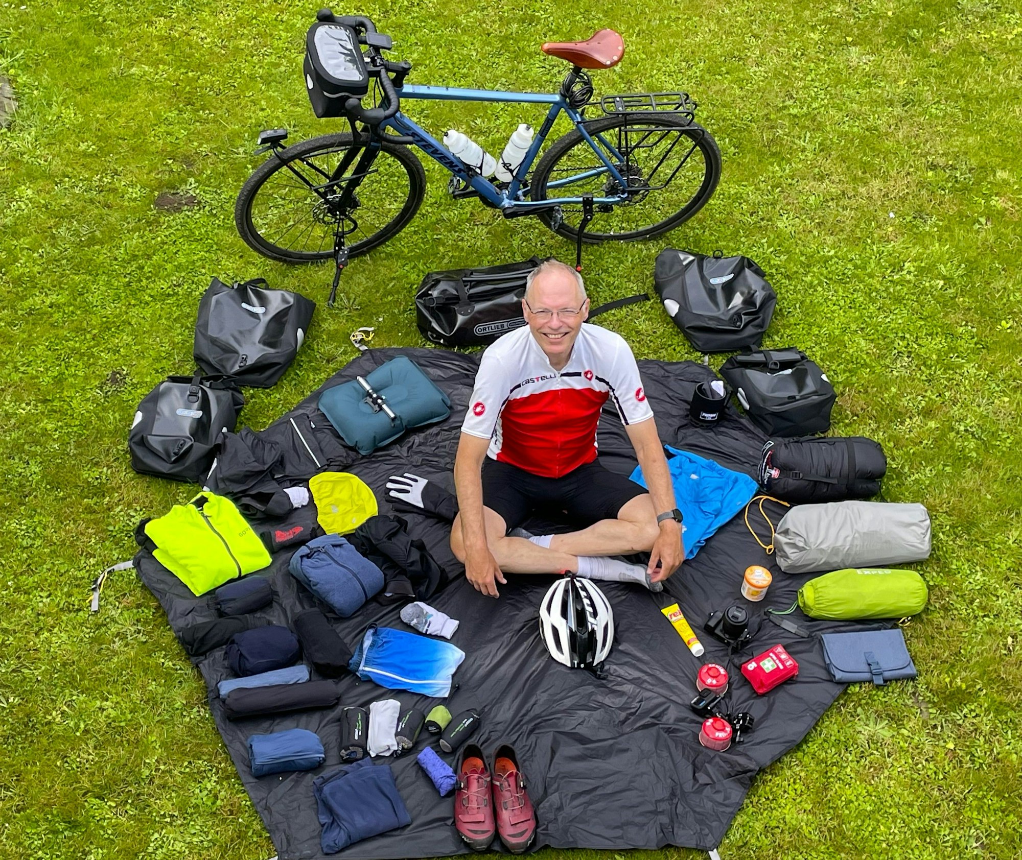 Johannes Hofmann sitzt auf der Wiese in seinem Weißer Garten. Um ihn herum verteilt liegt sein Gepäck.