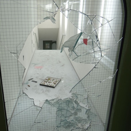 Eine zerschlagene Glastür und ein verwüsteter Gang zeigen das Ausmaß von Vandalismus in einer Schule.