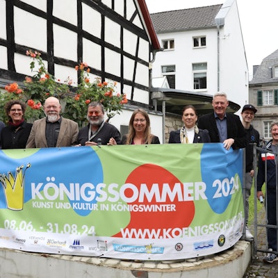 Eine Gruppe von Männern und Frauen stehen hinter einem Transparent mit der Aufschrift „Königssommer 2024“.