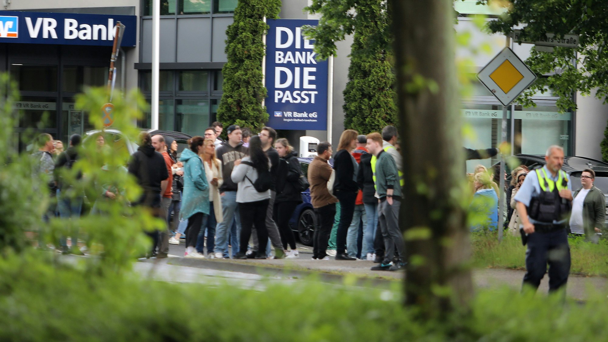Menschen warten auf dem Gehweg neben der Bensberger Straße.