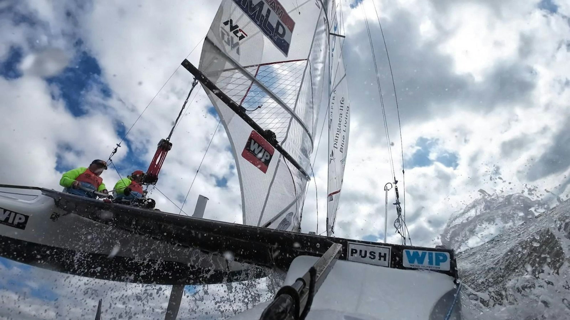 Ein Segelboot in Action: Zwei Personen sitze auf dem Segler, an den Seiten spritzt das Wasser.