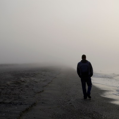Ein Mann, von dem nur die Umrisse zu erkennen sind, spaziert an einem nebeligen Strand entlang. (Symbolbild)