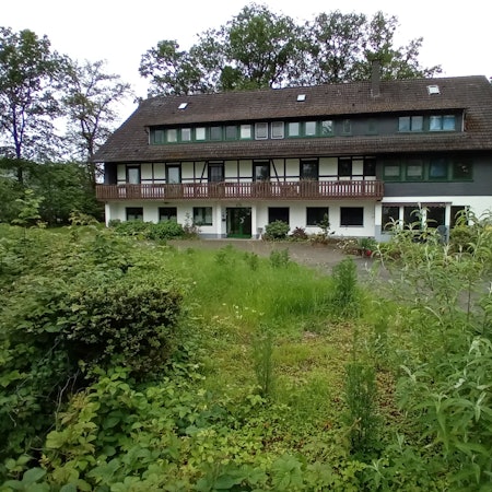 Ein dreigeschossiges Haus in einem verwilderten Garten.
