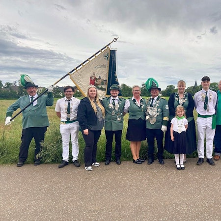 Mitglieder des Schützenvereins von Mülheim-Wichterich posieren in Uniform und mit Flagge vor einem Feld.