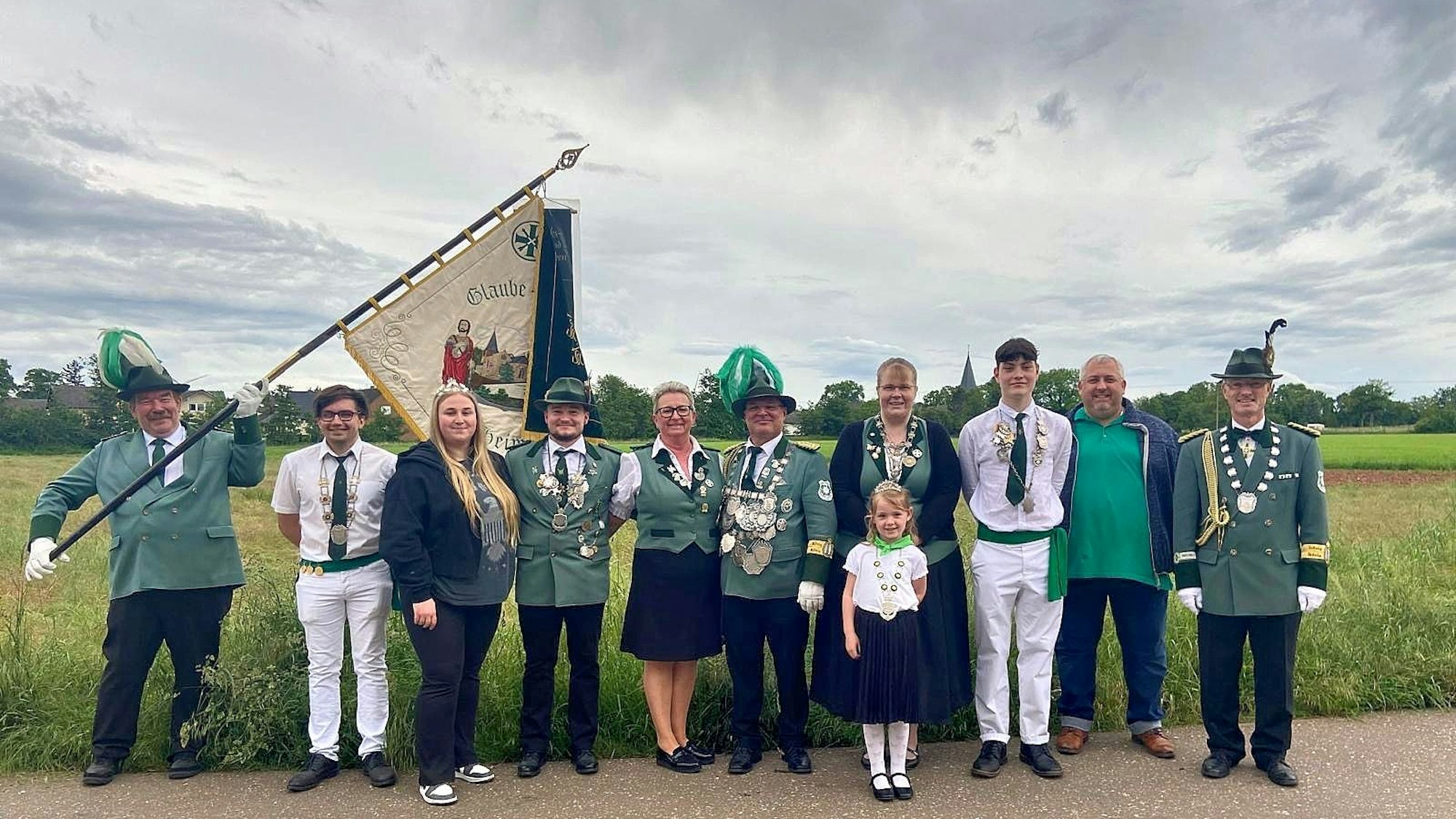 Mitglieder des Schützenvereins von Mülheim-Wichterich posieren in Uniform und mit Flagge vor einem Feld.