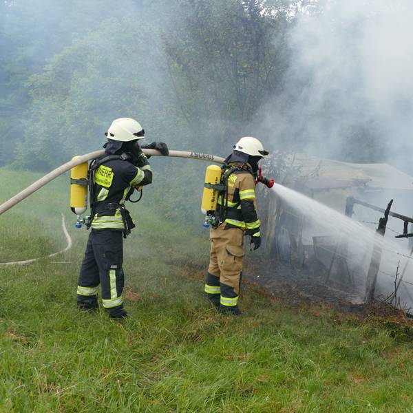 Feuerwehrleute löschen unter Atemschutz den niedergebrannten Wohnwagen.
