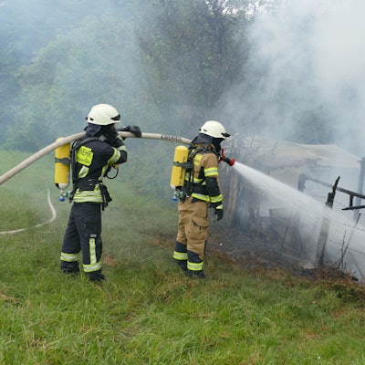 Feuerwehrleute löschen unter Atemschutz den niedergebrannten Wohnwagen.