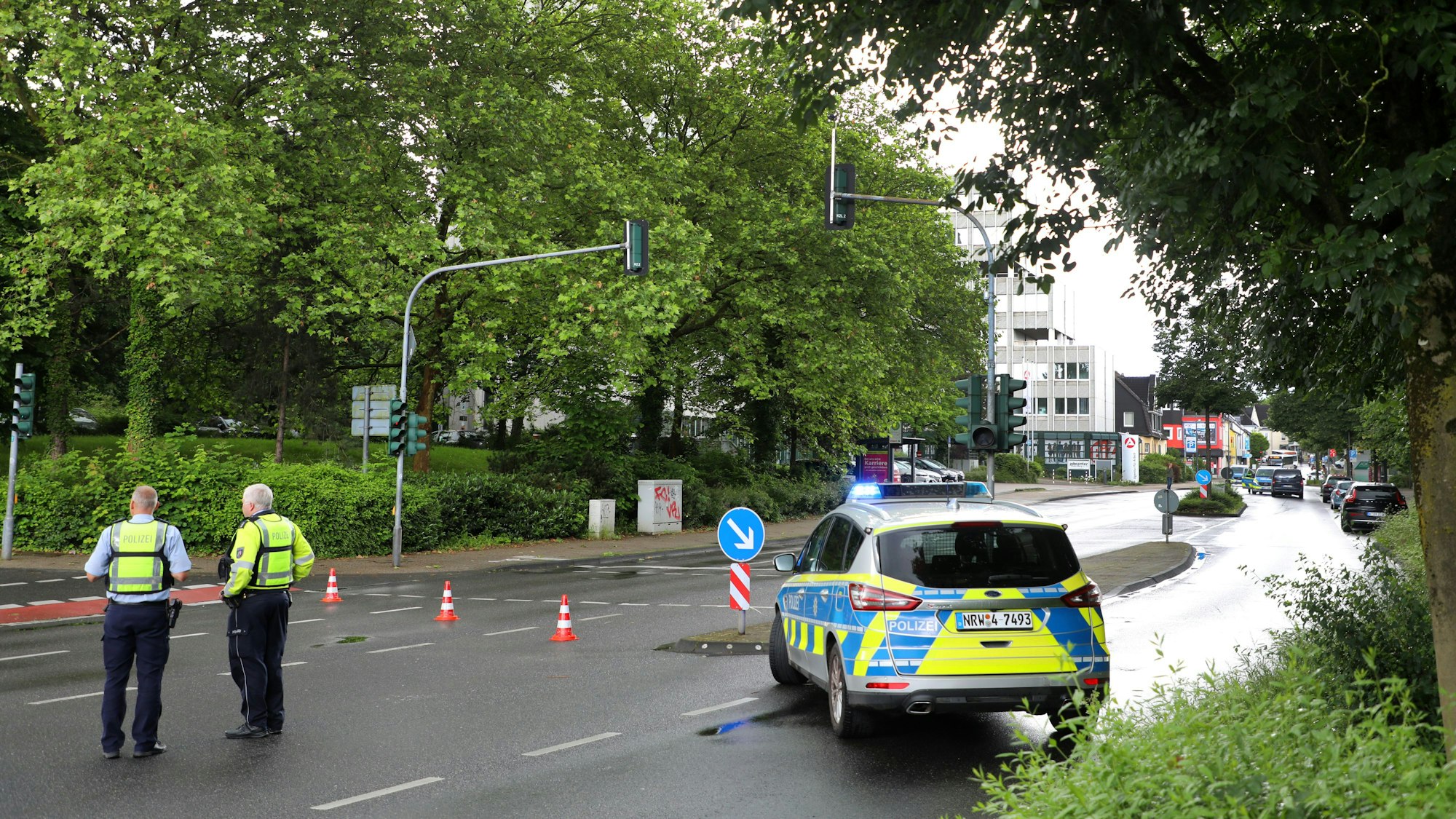 Ein Polizeifahrzeuge und Polizisten mit Pylonen haben die Bensberger Straße abgesperrt.