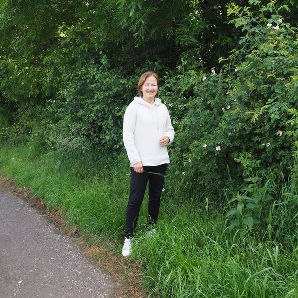 Petra Augel steht vor einem blühenden Rosenstrauch.