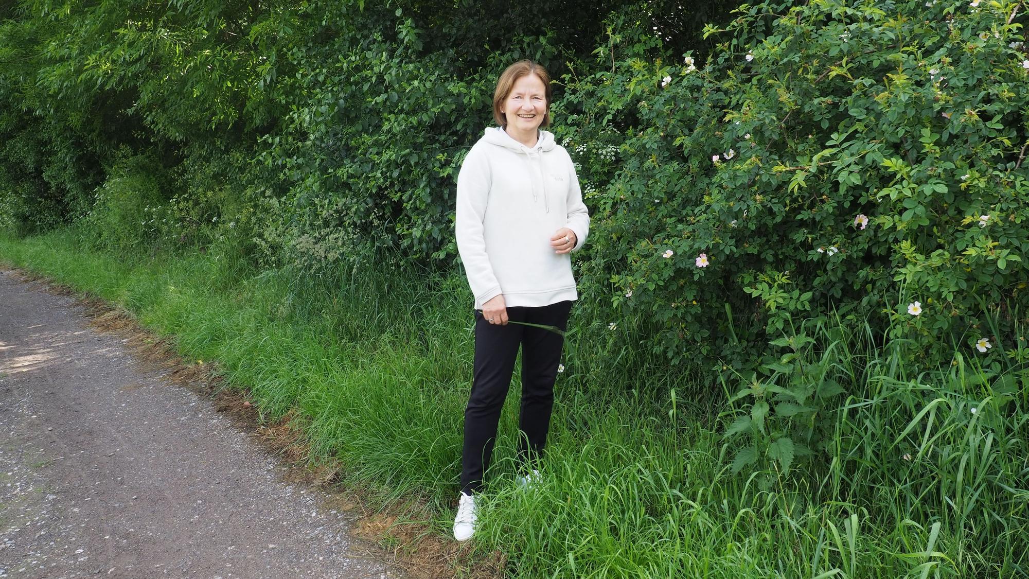 Petra Augel steht vor einem blühenden Rosenstrauch.