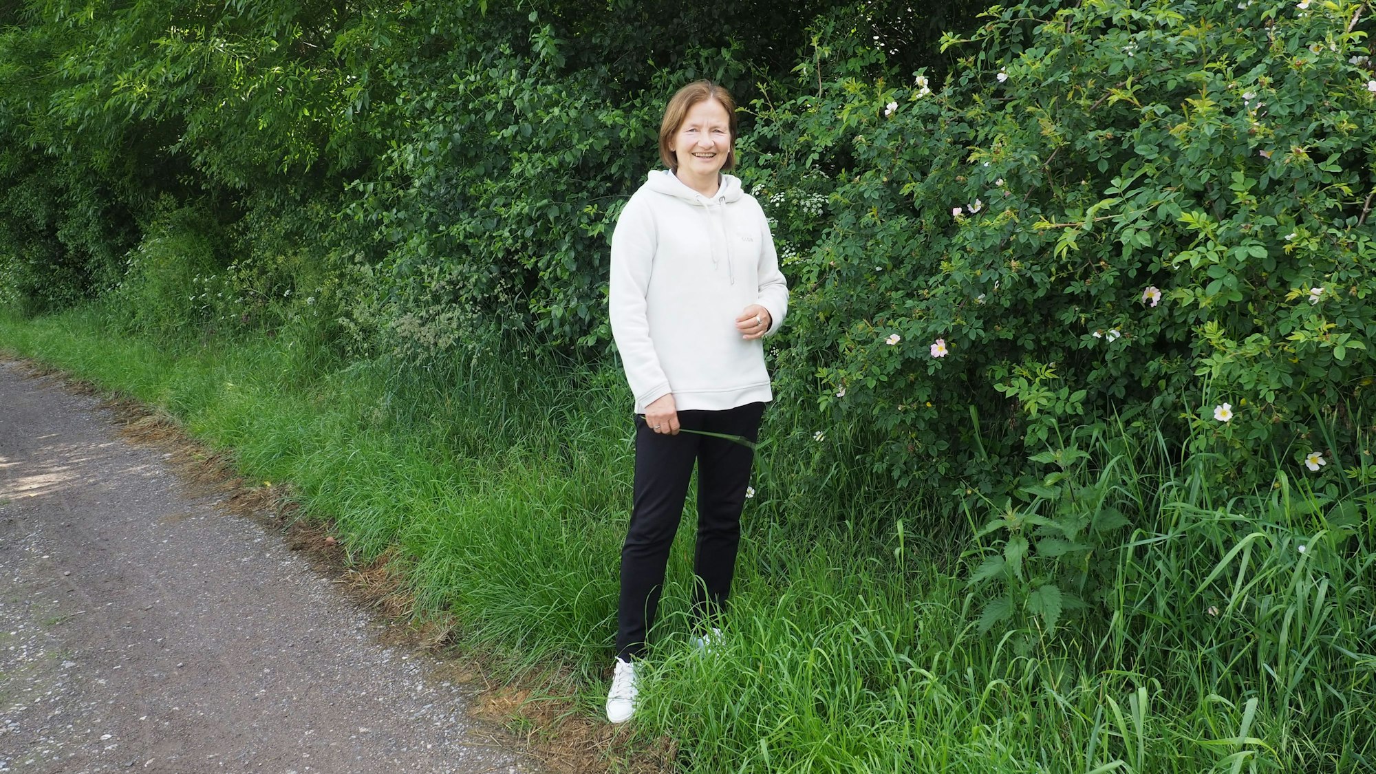 Petra Augel steht vor einem blühenden Rosenstrauch.