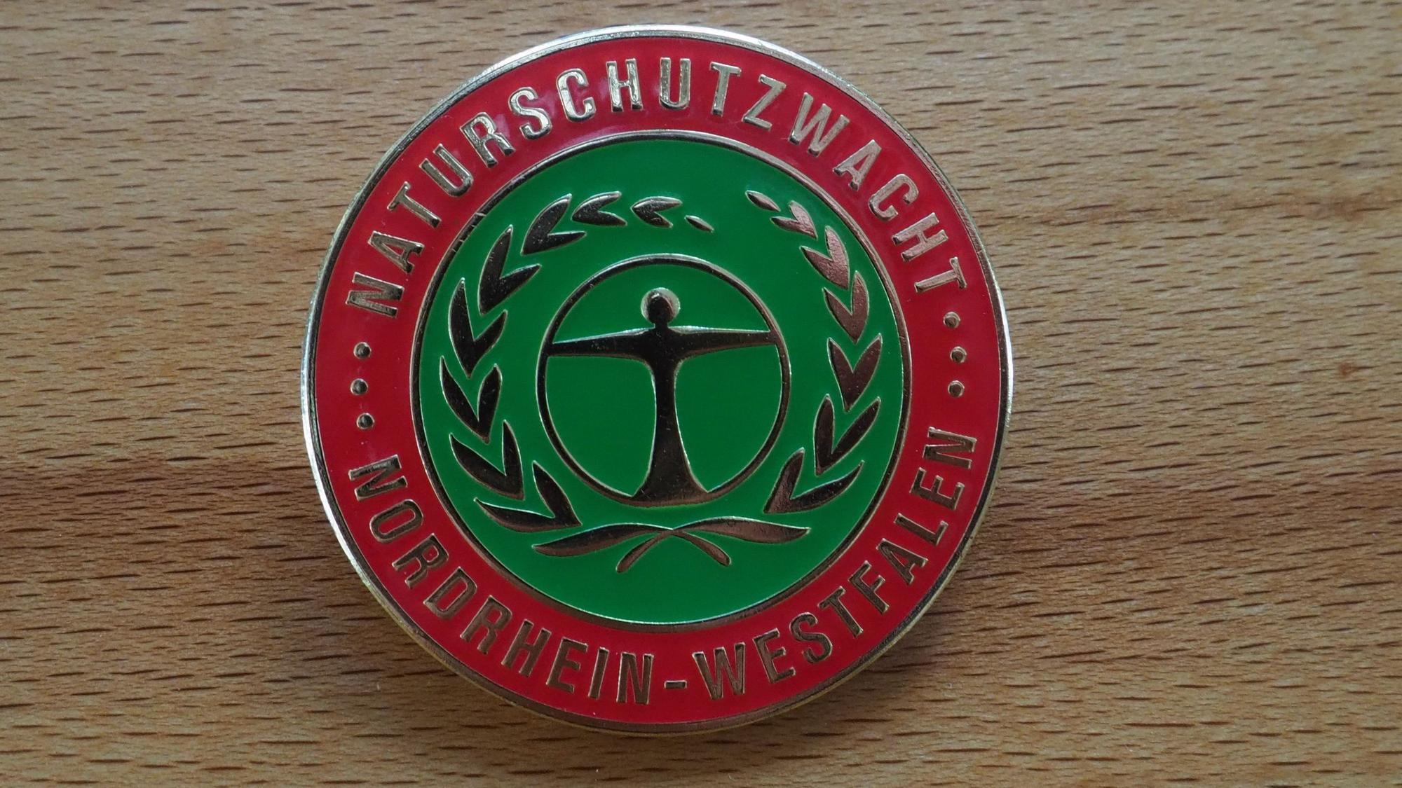 Auf einer runden Anstecknadel steht „Naturschutzwacht Nordrhein-Westfalen“.