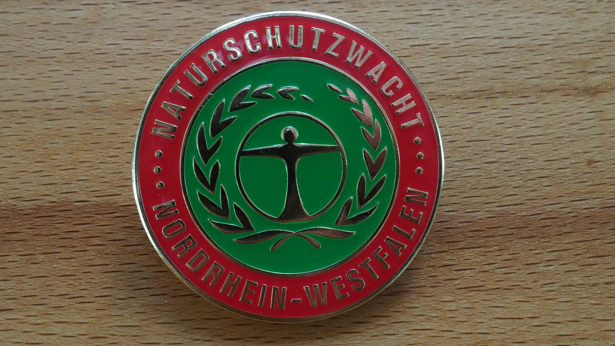 Auf einer runden Anstecknadel steht „Naturschutzwacht Nordrhein-Westfalen“.