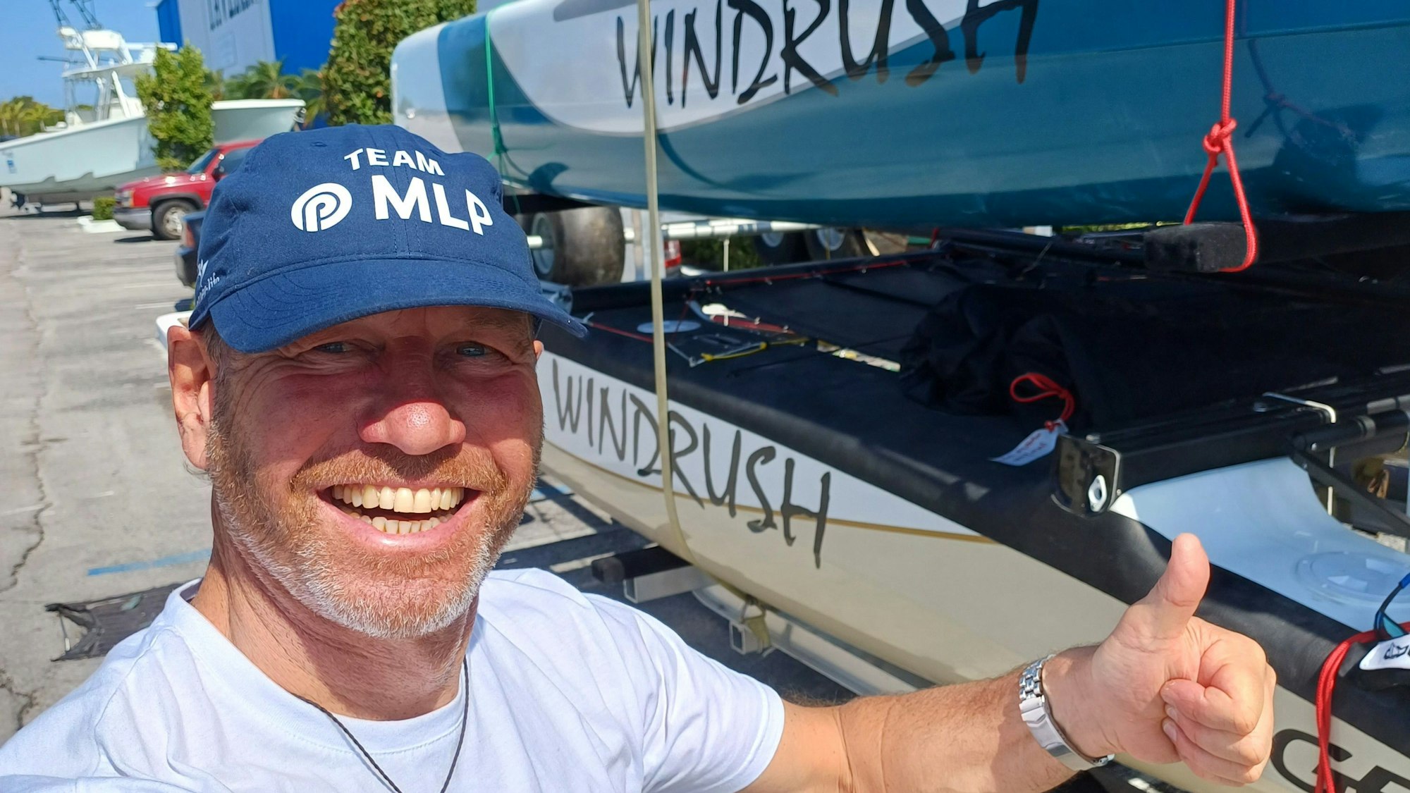 Multisportler André Hauschke lacht in die Kamera und reckt vor seinem Boot den Daumen in die Luft.