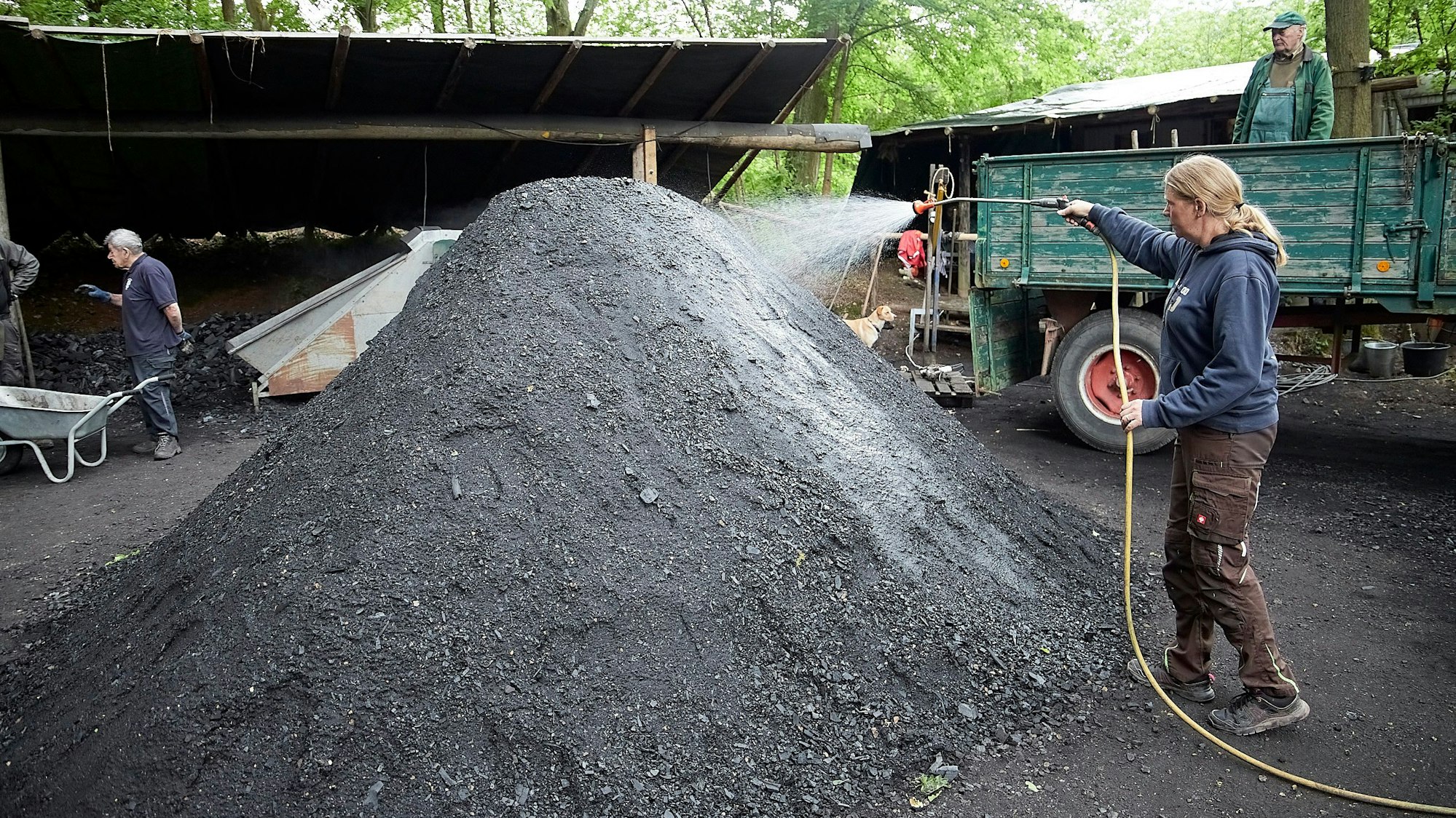 Mit einem Gartenschlauch wird Wasser auf einen Kohlehaufen gespritzt, um ihn zu befeuchten.
