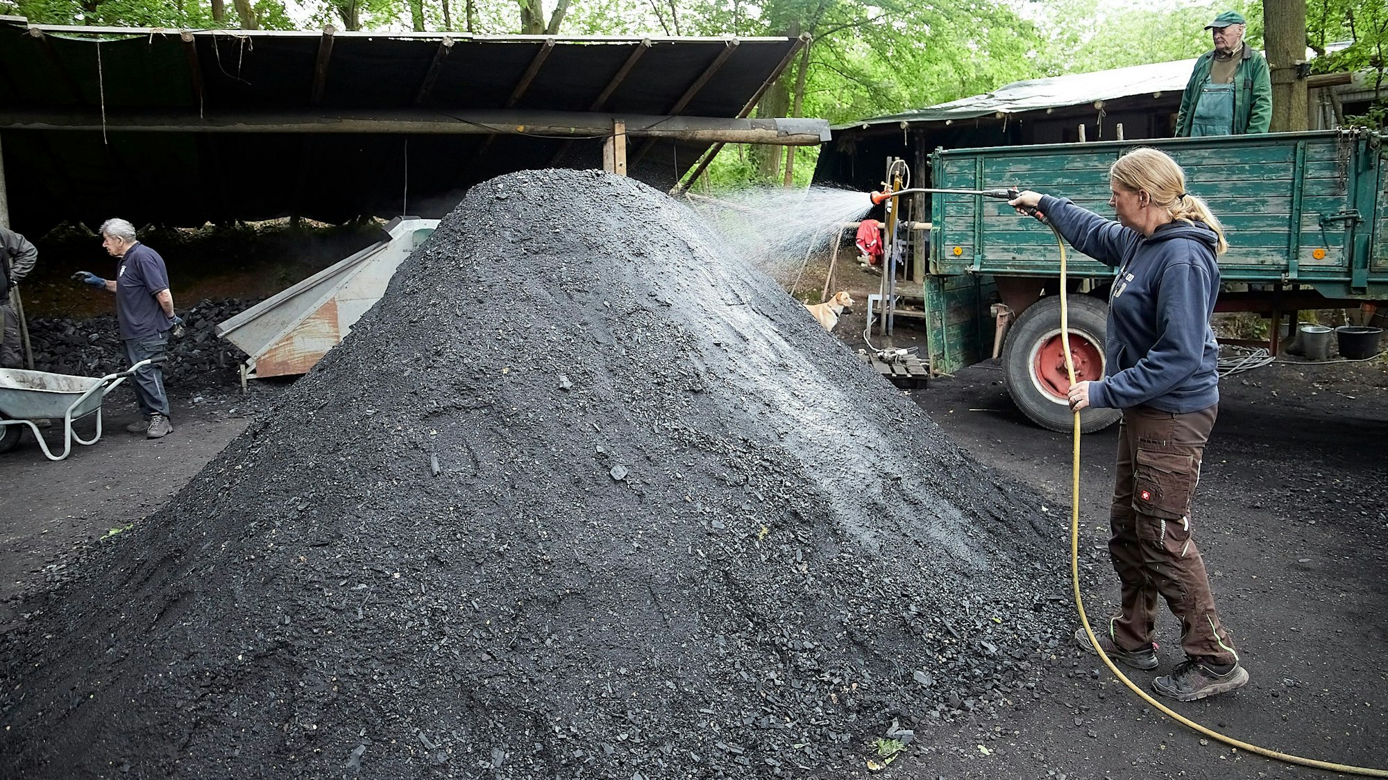 Mit einem Gartenschlauch wird Wasser auf einen Kohlehaufen gespritzt, um ihn zu befeuchten.