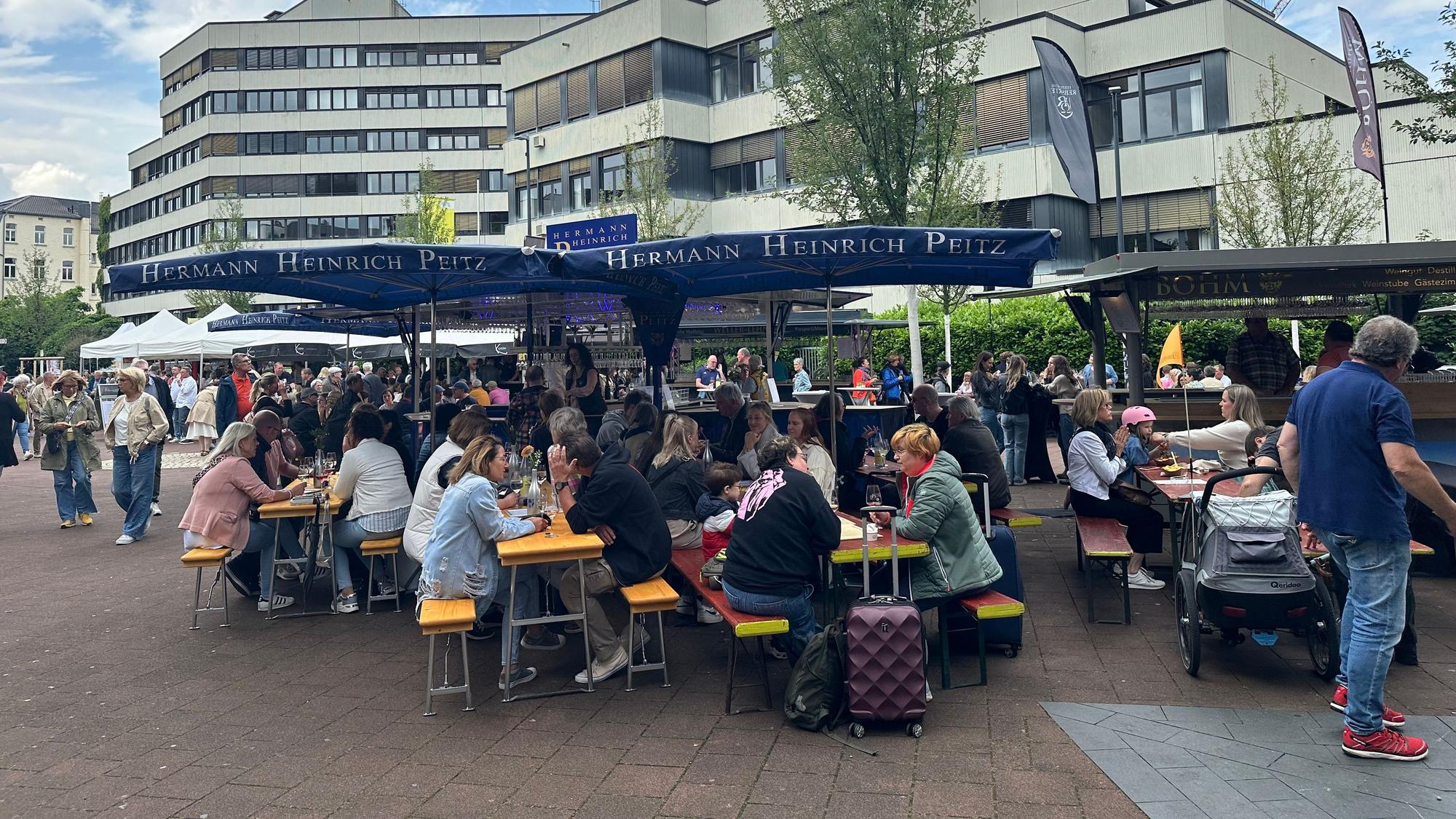 Menschen sitzen beim Weinfest in Siegburg auf Bierbänken.