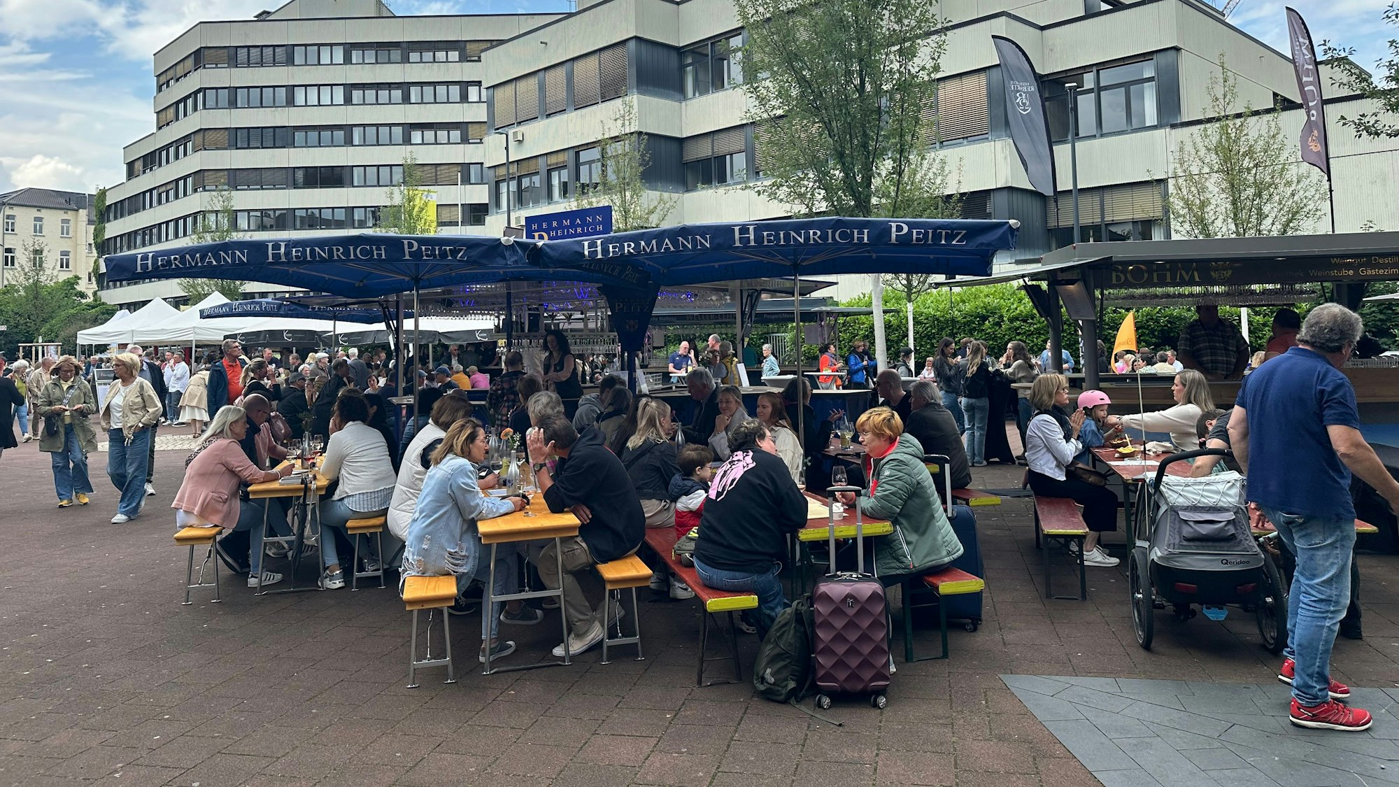 Menschen sitzen beim Weinfest in Siegburg auf Bierbänken.