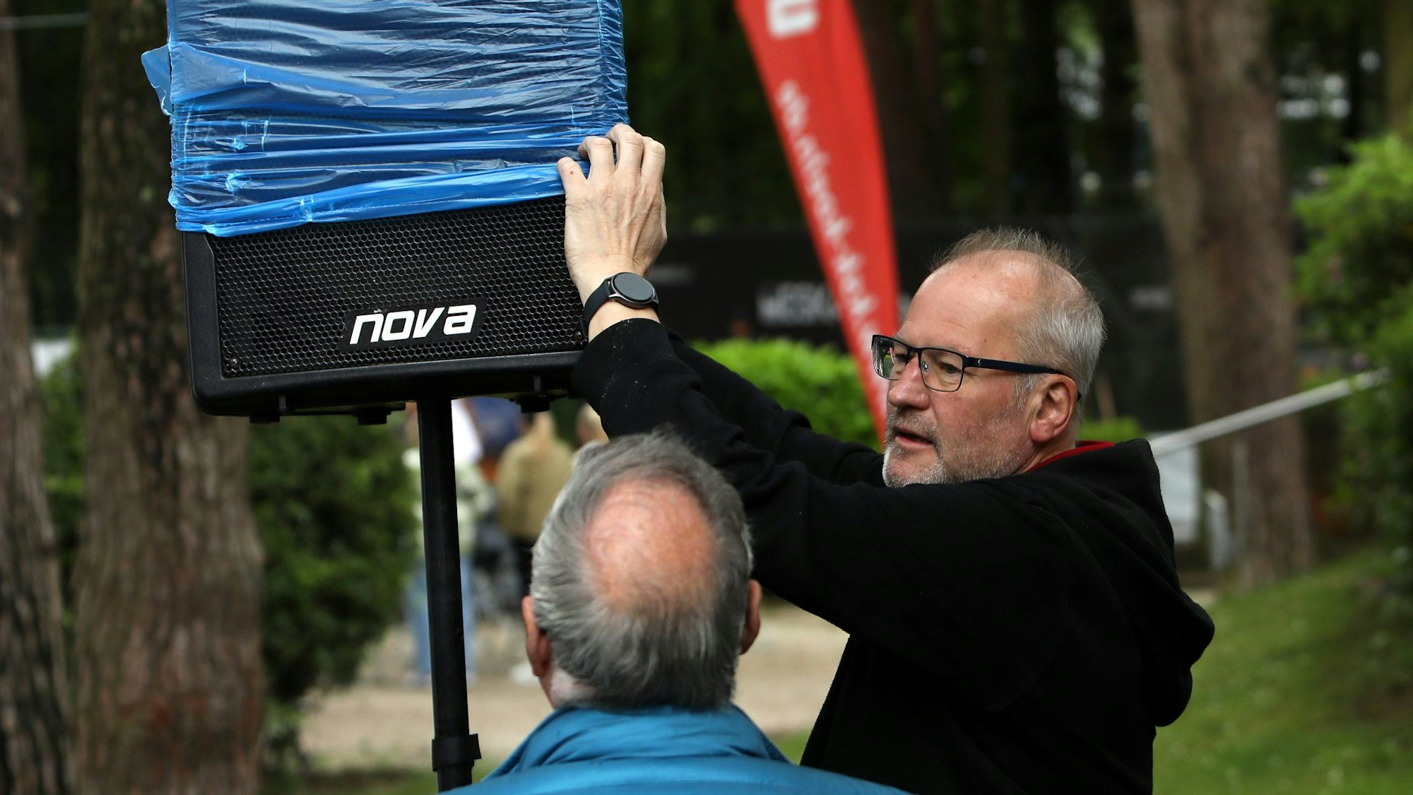 Ein Mann überzieht einen Lautsprecher mit einem blauen Plastikbeutel.