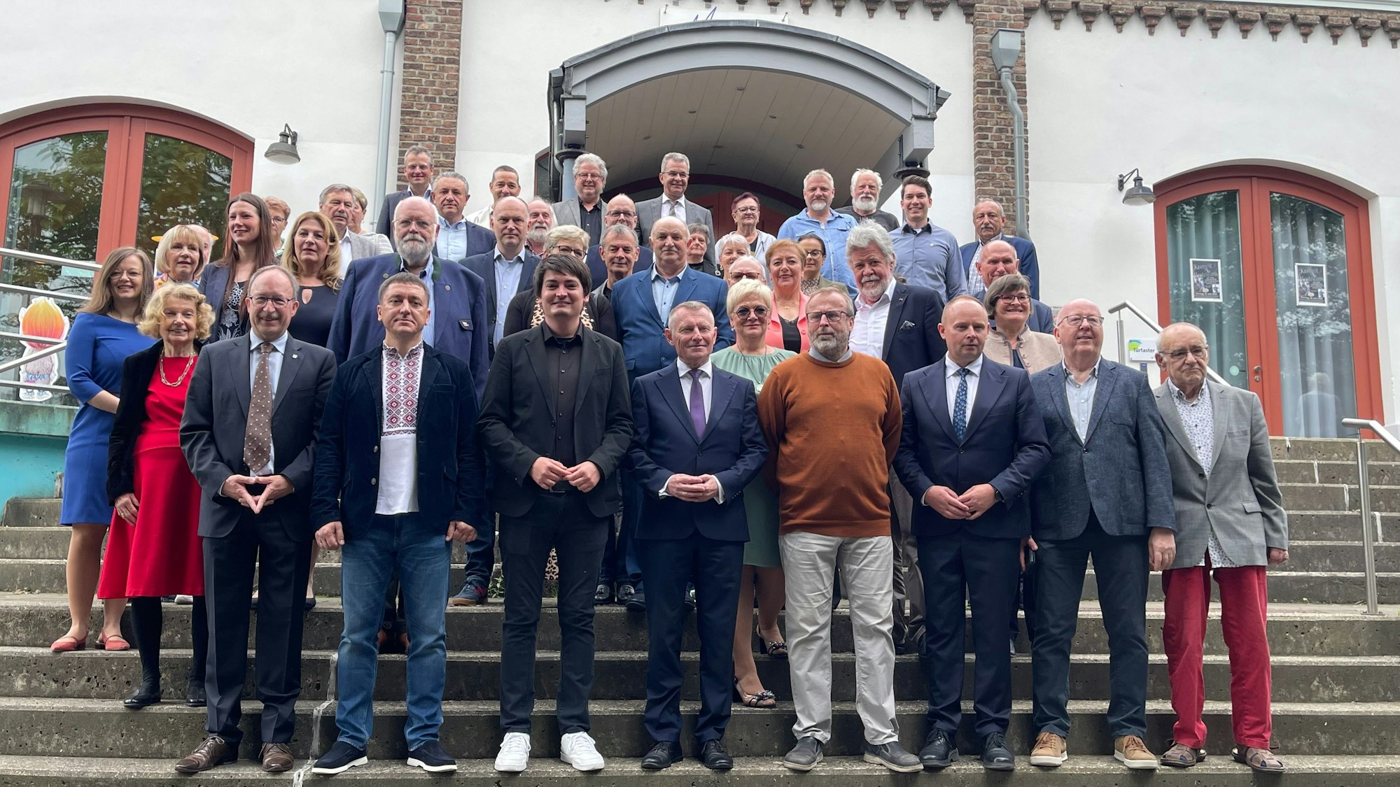 Eine Gruppe von Männern und Frauen steht auf einer Treppe vor einem Gebäude.