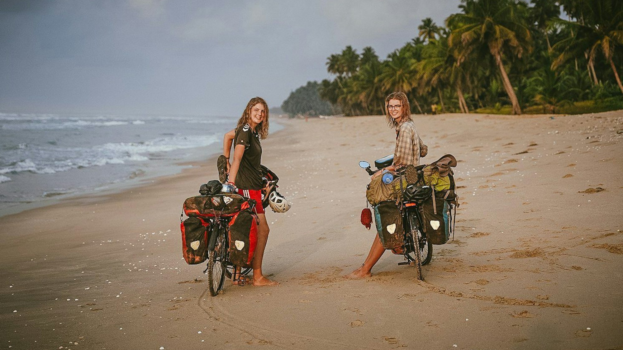 HANDOUT - 06.01.2024, Ghana, ---: Hannah (links) und Greta Schröder stehen mit ihren Fahrrädern an einem Strand in Ghana.