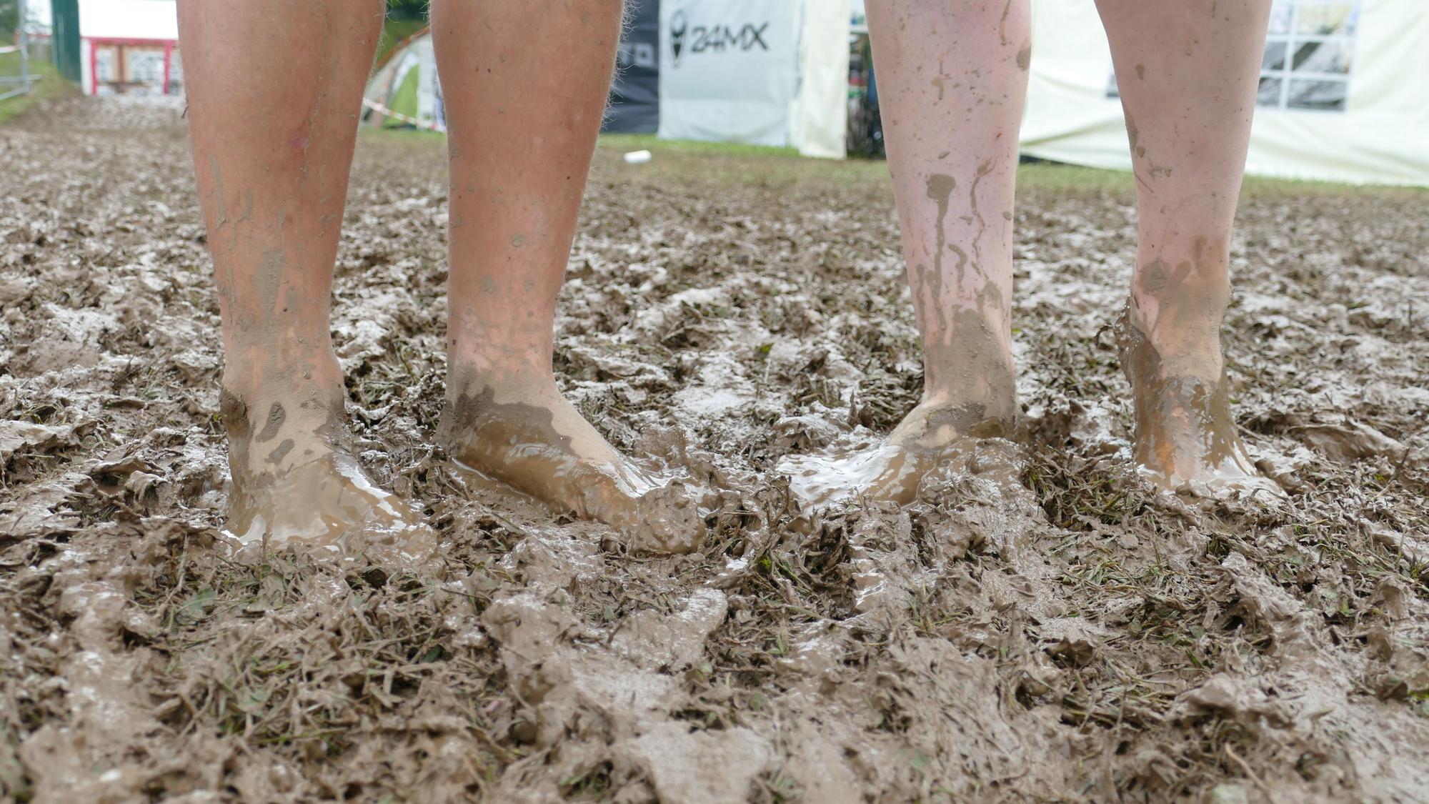 Vier nackte Beine stehen bis zu den Knöcheln im Matsch.