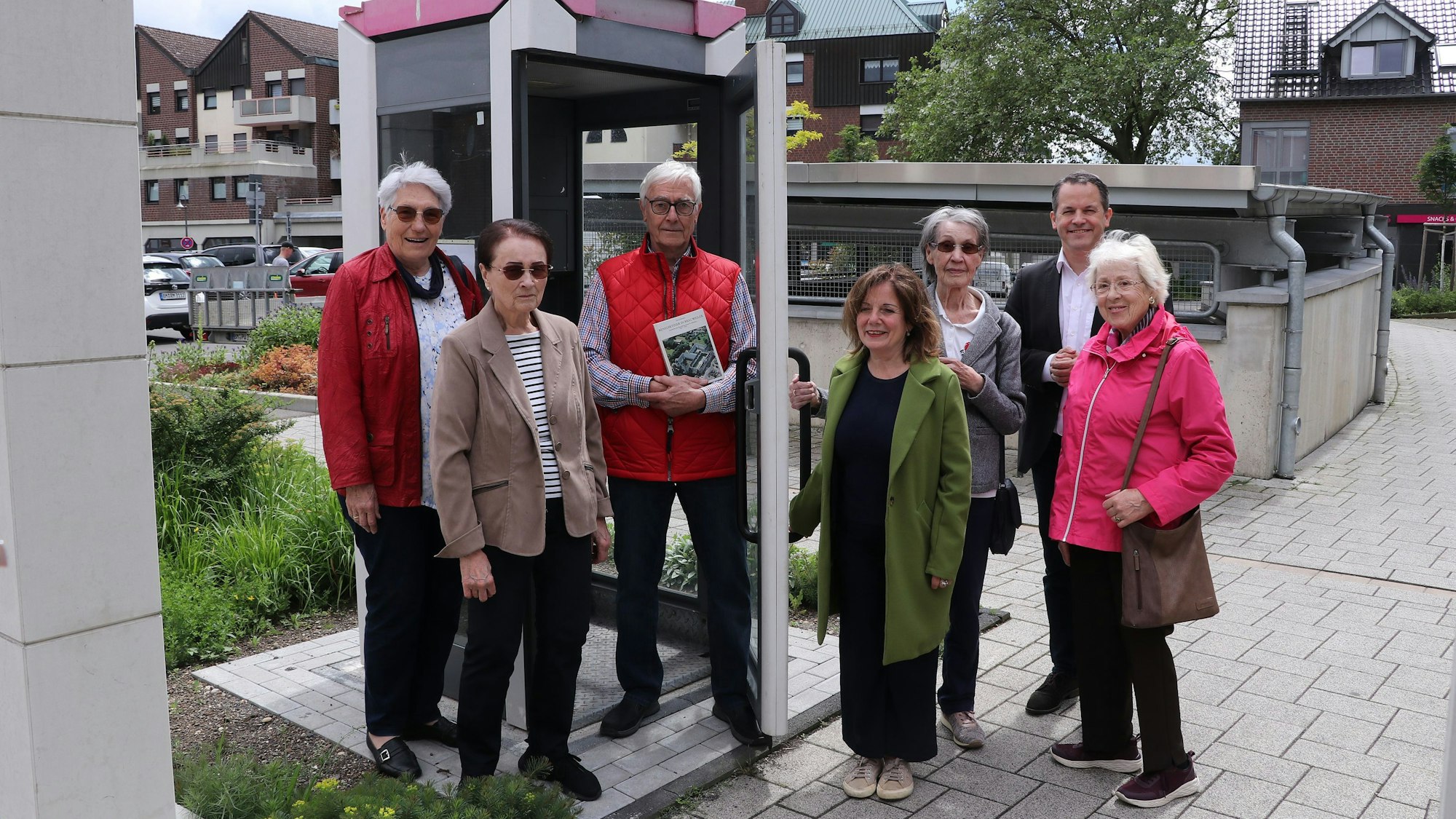 Sieben Personen stehen an einer alten, instand gesetzten Telefonzelle.