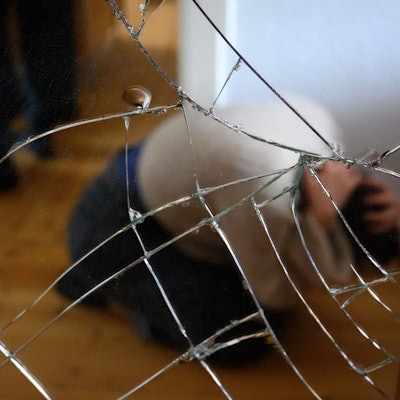 Ein Mann steht neben einer Frau, die am Boden mit ihren Händen ihren Kopf schützt (Illustration).