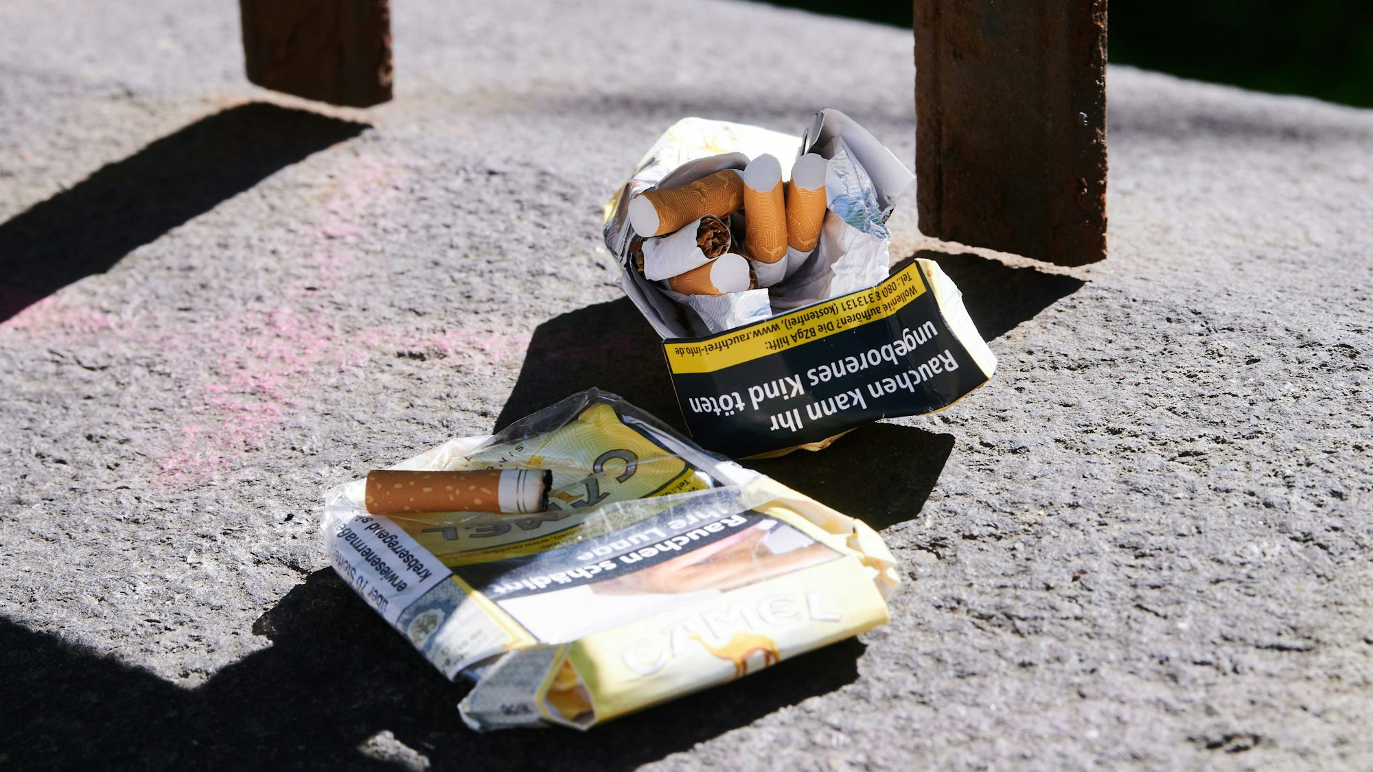 Zwei zerknüllte Zigarettenpackungen liegen auf einer Mauer.