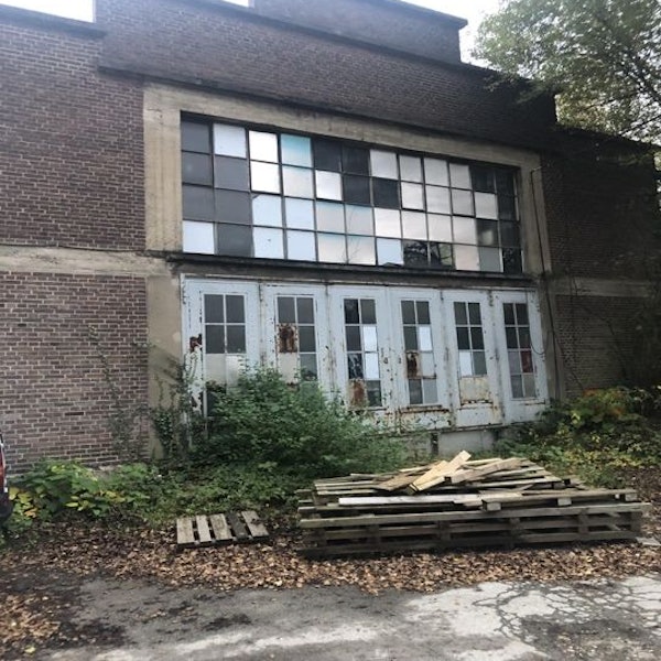 Runtergekommene Gebäudefront eines Ziegelbaus. Davor liegen Holzlatten gestapelt.