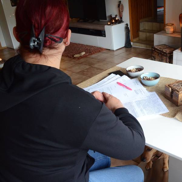 Eine Frau sitzt an einem Tisch, sie hat Briefe und Gutachten vor sich auf dem Tisch liegen.