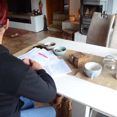 Eine Frau sitzt an einem Tisch, sie hat Briefe und Gutachten vor sich auf dem Tisch liegen.