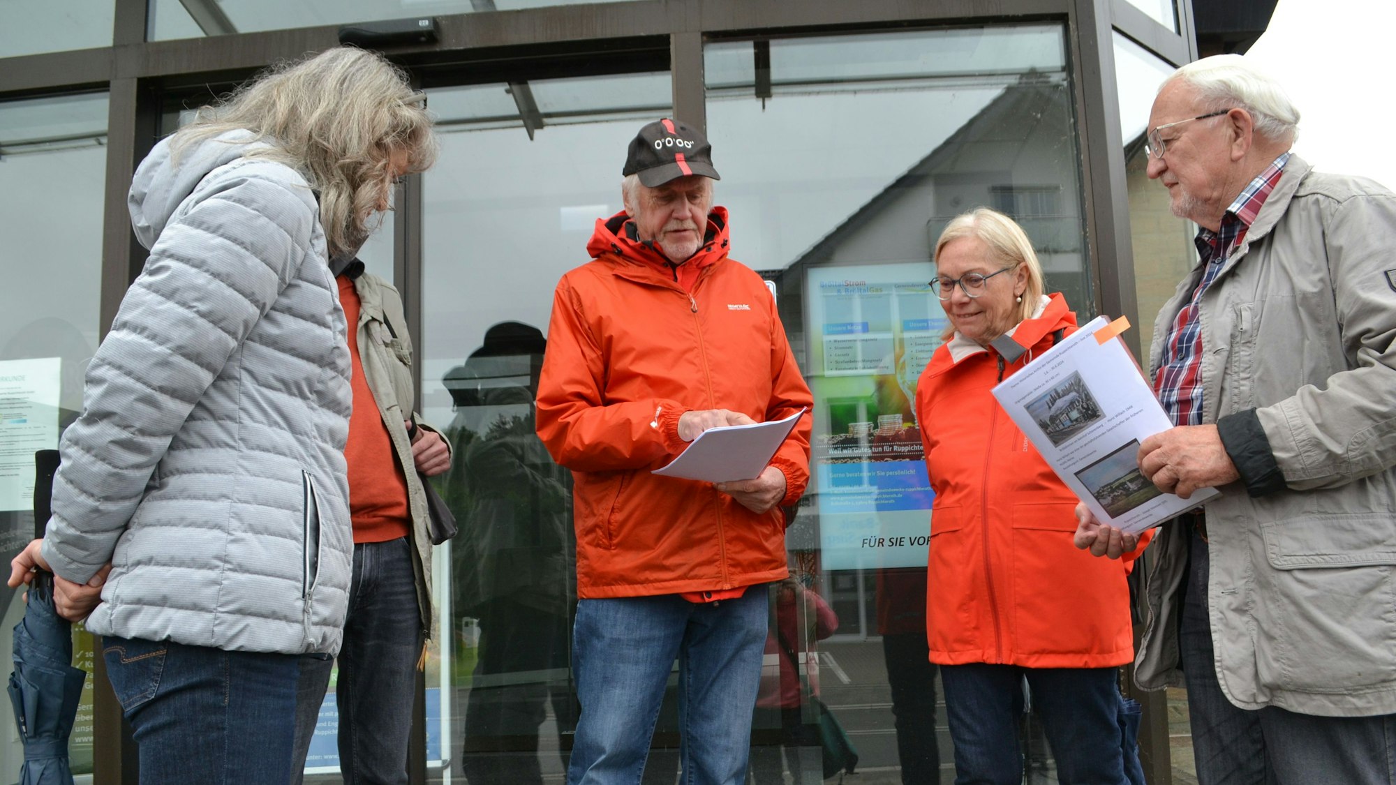 Männer und Frauen in wetterfester Kleidung vor einem verglasten Gebäudeeingang.