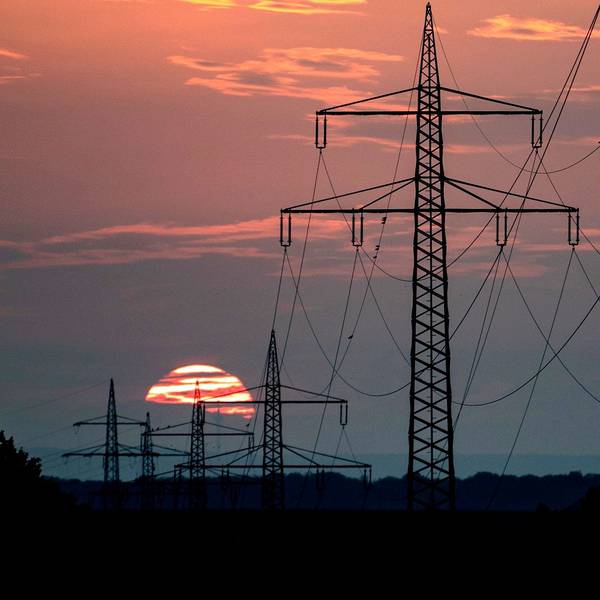 Im Sonnenuntergang sind einige Strommasten und Leitungen zu sehen. Die Sonne hat die Wolken rosa gefärbt.